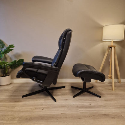 Stressless View lenestol i svart skinn sett fra siden i oppreist sittestilling, med krakk